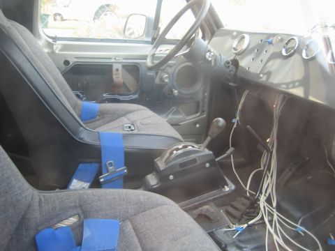1990 Ford Bronco - stripped truck interior with gray cloth seats taped in blue, a floor shifter and bundles of exposed wiring along the door.
