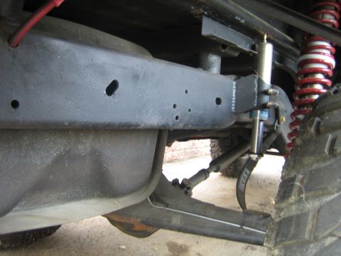 1990 Ford Bronco - Underside view of a vehicle's frame rail showing a red coilover spring, blue shock and steering linkage over a concrete floor.