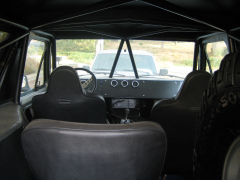 1990 Ford Bronco - Vehicle interior with a black roll cage, two bucket seats and floor shifter, an exterior spare tire visible through a side opening.