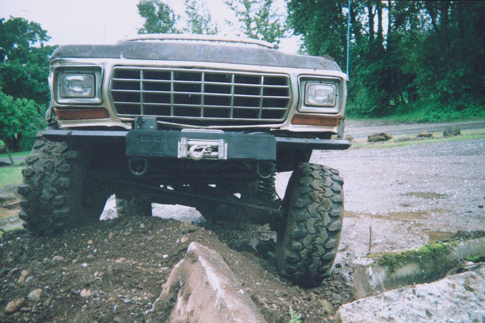 Front of lifted vintage Ford truck with winch bumper on big mud tires over a dirt mound