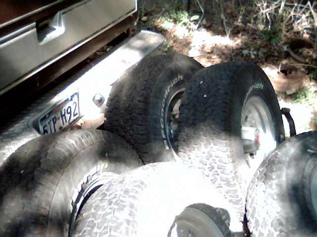 Spare tires piled up next to a vehicle's rear bumper and license plate reading 6TP H92