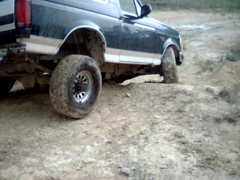 1992 Ford Bronco - A 1992 Ford Bronco navigates an off-road trail, its tires covered in mud.