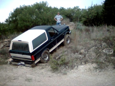 1992 Ford Bronco - A 1992 Ford Bronco navigates a rocky, off-road trail with a person standing in the background.
