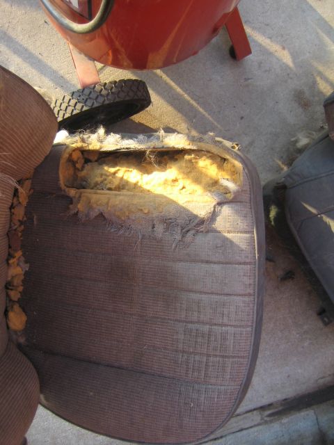 1990 Ford Bronco - worn brown vehicle seat cushion lies on concrete with its upholstery torn open to reveal crumbling yellow foam padding.
