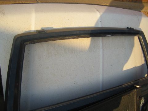 1990 Ford Bronco - Close-up of a dirty white vehicle body panel and the black-trimmed rear quarter window glass.