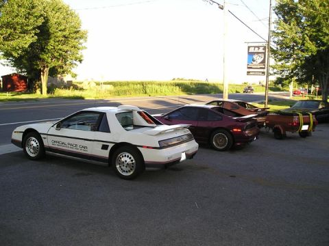 1984 Pontiac Fiero - Several Pontiac Fieros are lined up, including a white pace car, with a pickup truck in the background.