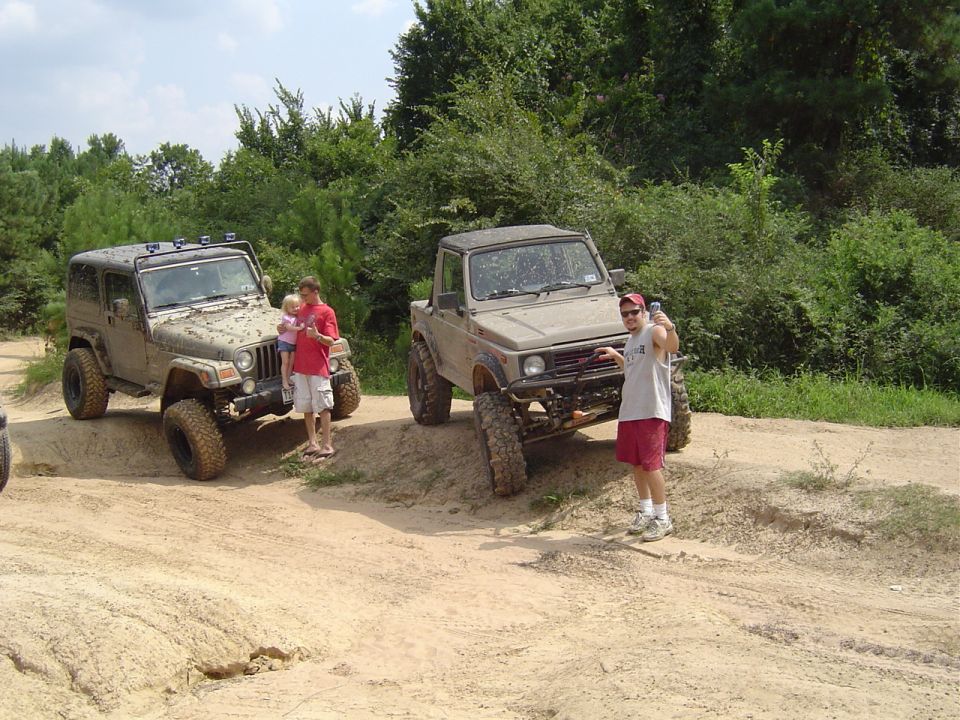 Lifted Jeep Wrangler and a Suzuki Samurai on muddy dirt trail with people standing by