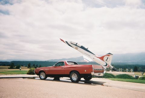 1972 Ford Ranchero - A red 1972 Ford Ranchero is parked beside a U.S. Air Force jet display under a cloudy sky.