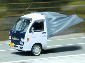 1988 Ford Bronco - A small white truck is captured in motion, its cargo covered by a flapping tarp.
