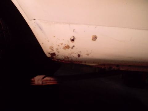 1966 Ford Fairlane - Close-up of rust damage on a white vehicle's lower body panel, with a leaf spring visible underneath.