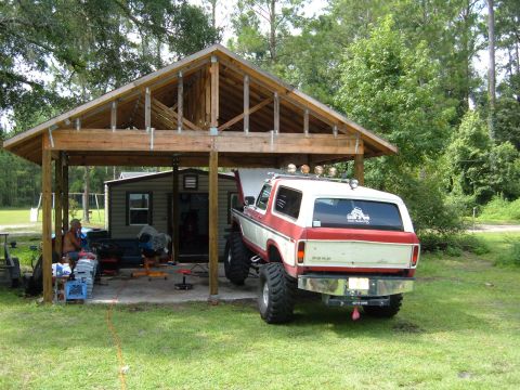 1978 Ford Bronco - This red and white 1978 Ford Bronco, modified with large tires, is parked under a carport with its hood open.