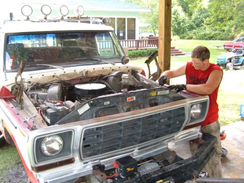 1978 Ford Bronco - A man works on the engine of a 1978 Ford Bronco, which has its hood open and the engine compartment visible.