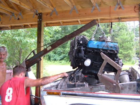 1978 Ford Bronco - Mechanics work on an engine swap, with the engine suspended by a crane.