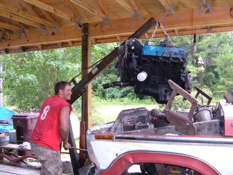 1978 Ford Bronco - A man operates a crane to lift an engine into the open bay of a truck.