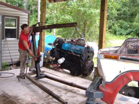 1978 Ford Bronco - Engine hoist lifting a V8 engine beside a truck's front end.