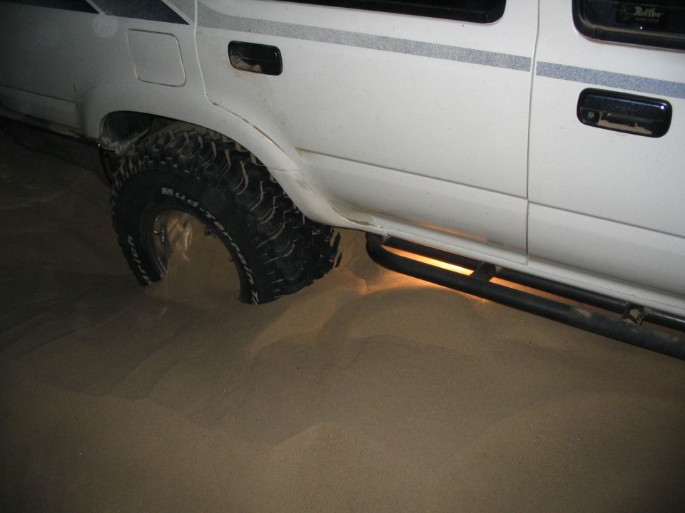 White lifted truck with mud tires sunk into sand at night, tube rocker visible