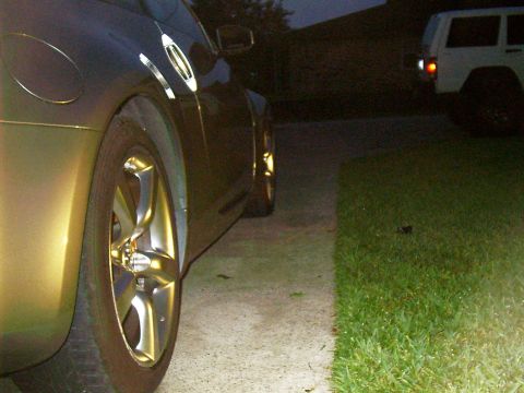 1986 Ford Bronco - Gold car side view with chrome wheels and a white SUV in the background at dusk.
