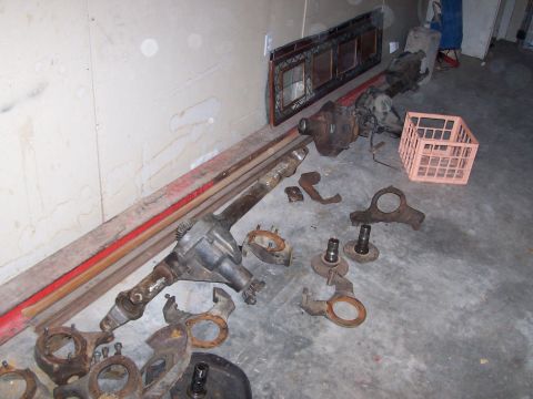 1991 Ford Bronco - Various vehicle axle and suspension parts are laid out on a concrete floor next to a wall.