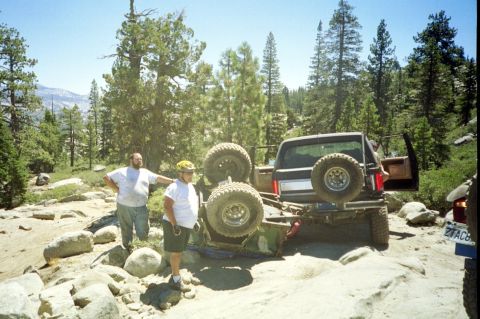 1967 Ford Bronco - An off-road SUV is stuck on rocks with its rear end lifted, while two men observe the scene.