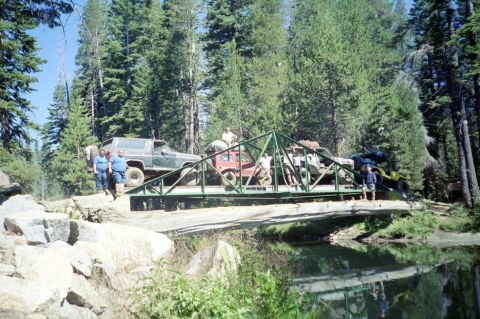1967 Ford Bronco - Multiple off-road vehicles traverse a bridge in a wooded area.