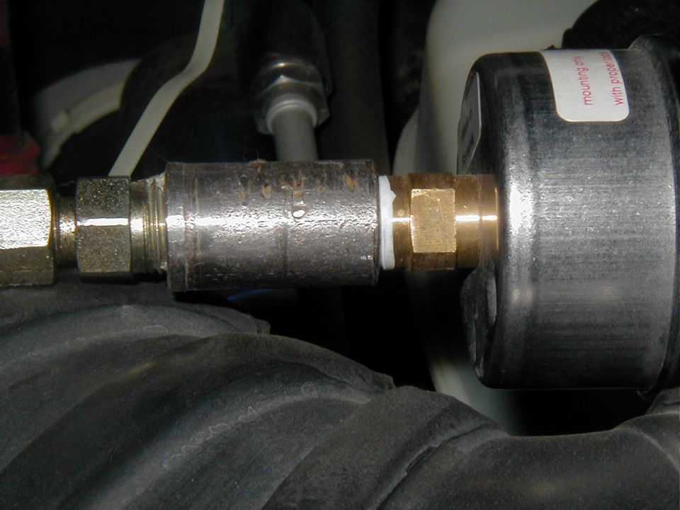 Close-up of brass fittings and inline filter threaded into a black canister in an engine bay
