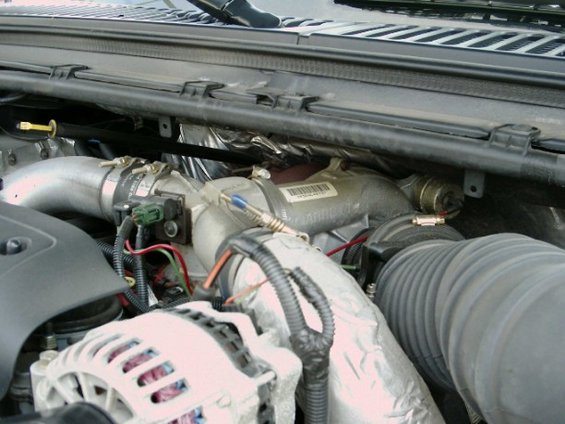 Top-down view of engine valley with intake manifold, alternator, and barcode label on a casting
