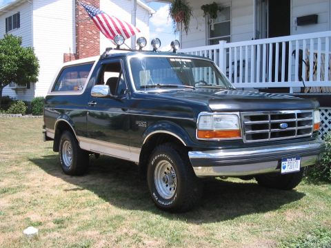 1992 Ford Bronco - A dark green 1992 Ford Bronco with a white top and tan lower trim is parked on a grassy lawn in front of a house.