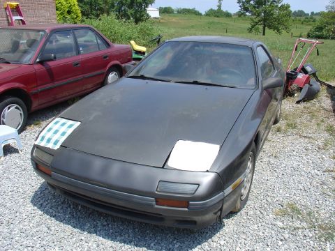 1993 Ford Probe - A dark gray Mazda RX-7 is parked next to a red sedan in a gravel lot.