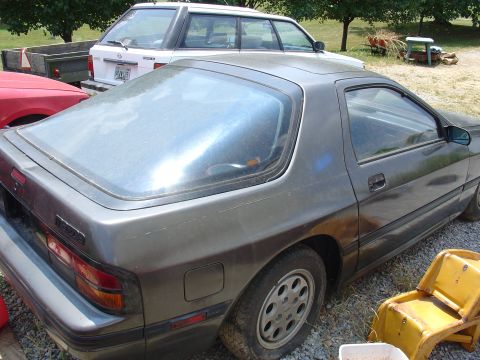 1993 Ford Probe - A Mazda RX-7 is parked outdoors next to other vehicles and a trailer.