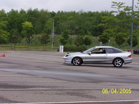 1993 Ford Probe - A silver 1993 Ford Probe is seen on a track during an event, with a driver wearing a helmet inside.