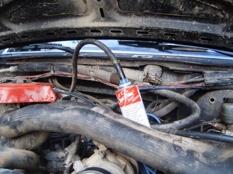 1988 Ford Bronco - A can of carburetor cleaner is attached to a hose in the engine bay of a vehicle.