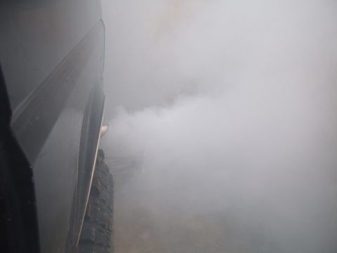 1988 Ford Bronco - Thick exhaust smoke obscures the view, originating from a vehicle's tailpipe.