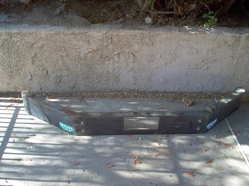 Weathered steel front bumper lying on concrete driveway against stucco wall