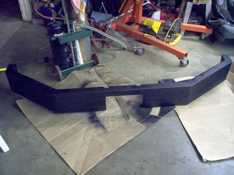 1988 Ford Bronco - A newly painted aftermarket bumper sits on cardboard in a workshop environment.