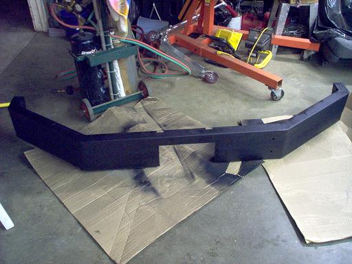 Black aftermarket bumper on cardboard in a garage with tools in the background
