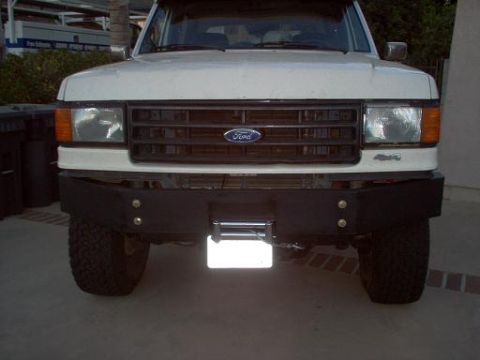1988 Ford Bronco - Head-on view of a white Ford truck fitted with a black fabricated tube-style front winch bumper and a recessed winch with roller fairlead b…