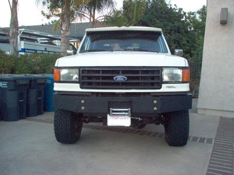 1988 Ford Bronco - Front view of a white Ford full-size truck/SUV with a black steel front bumper housing a winch, amber turn signals, chrome grille with Ford…