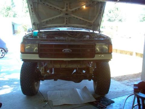 1988 Ford Bronco - Front view of a tan/cream Ford truck in a garage with the hood raised and the front bumper removed, exposing the frame horns, radiator supp…