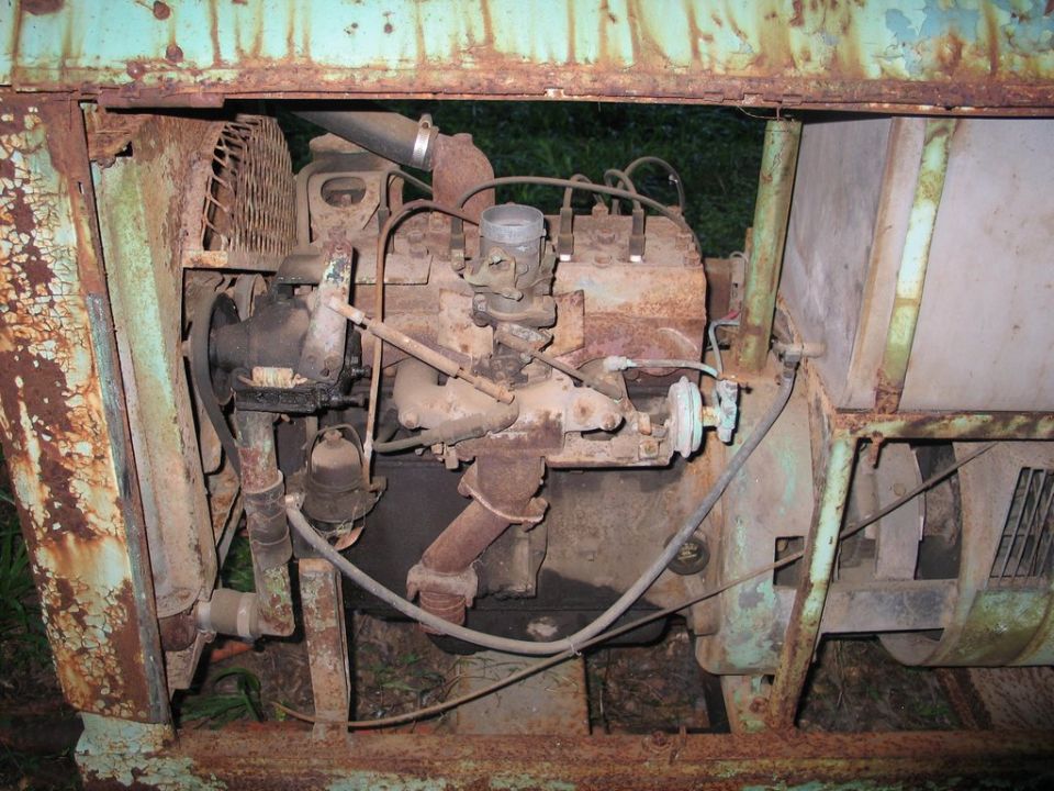 Rusty flathead four-cylinder engine inside a mint-green welder frame, carburetor and manifold visible