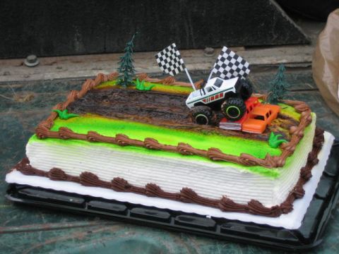 1987 Suzuki Samurai - A cake decorated with toy vehicles and checkered flags, resembling a race scene.