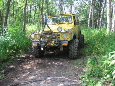 1987 Suzuki Samurai - Yellow 1987 Suzuki Samurai on a wooded trail, equipped for off-road use with large tires and snorkel.