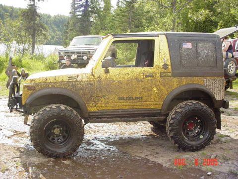 1987 Suzuki Samurai - Mud-covered yellow Suzuki Samurai parked outdoors with a second vehicle in the background.