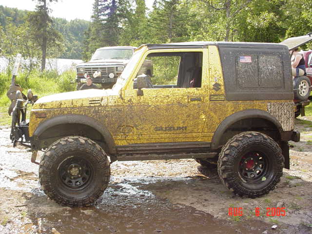 Mud-covered yellow Suzuki Samurai SUV in side view on lifted off-road tires