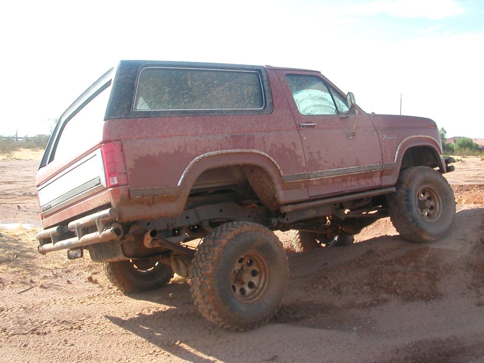 Lifted maroon Ford Bronco on mud tires parked in desert dirt, rear three-quarter view