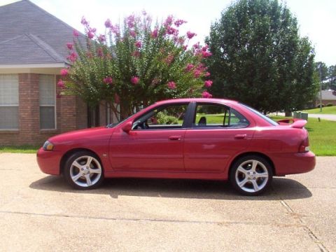 2002 Nissan SE-R - This red 2002 Nissan SE-R sedan is shown from the side, parked in front of a house with flowering trees.