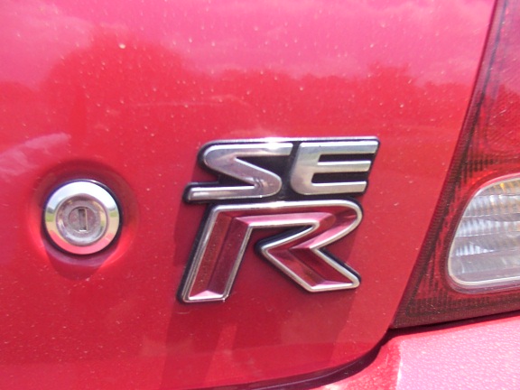 Chrome stacked SE-R badge on the red trunk lid of a sedan next to trunk lock