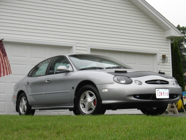 Silver Ford Taurus sedan parked on grass in front of a white garage with US flag