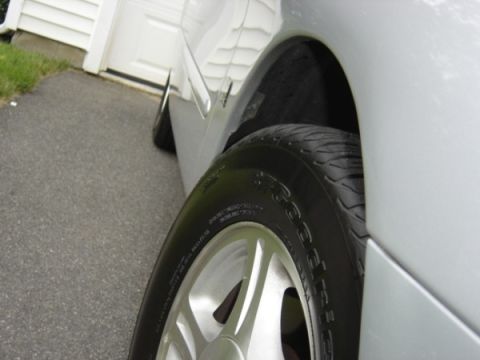 1999 Ford Taurus - Close-up of a silver car's wheel and fender against an asphalt driveway and garage door.
