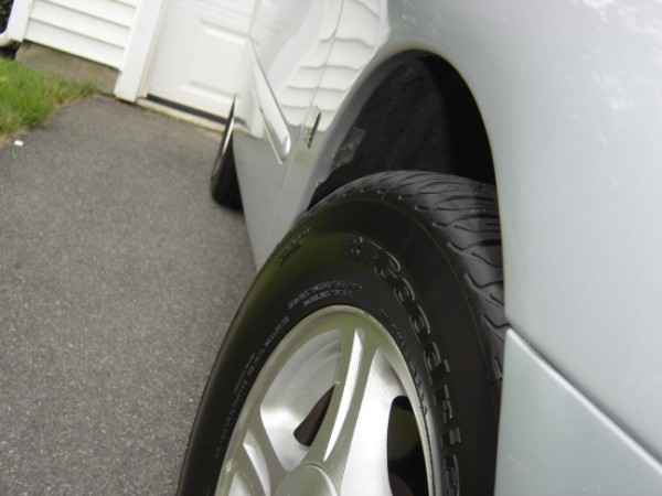 Silver car wheel and fender, close-up side view, asphalt driveway, white garage door in background