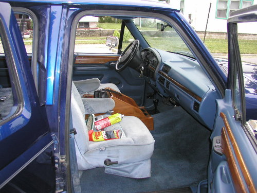 blue interior with light gray seats, dashboard, and wood trim. Cans on the passenger seat